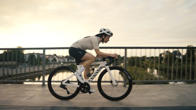 Radfahrer in sportlicher Kleidung fährt über eine Brücke bei Sonnenuntergang.