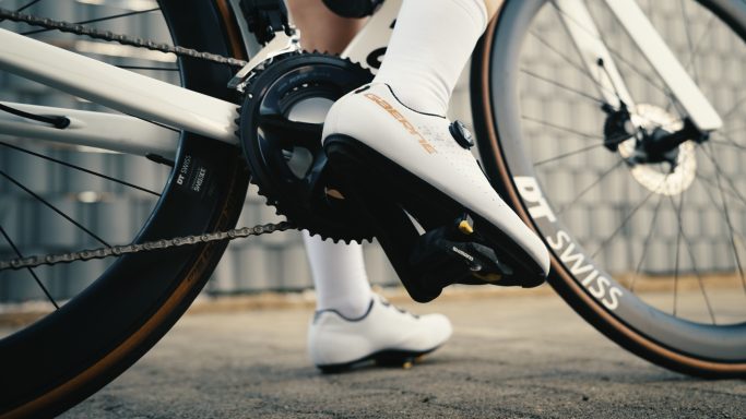 Nahaufnahme eines Fahrradpedals mit einem Radfahrer im Hintergrund.